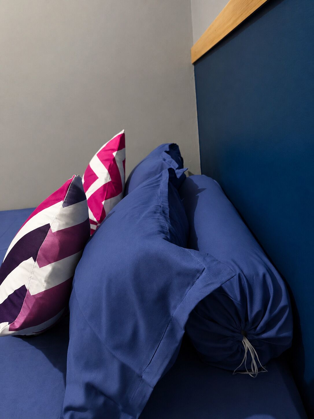 A bed with two pillows, one with a zigzag pattern and the other solid blue.