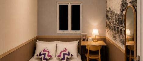 A bedroom with a bed, a desk, a chair, a mirror, an air conditioning unit, and a wall with a Paris-themed artwork.