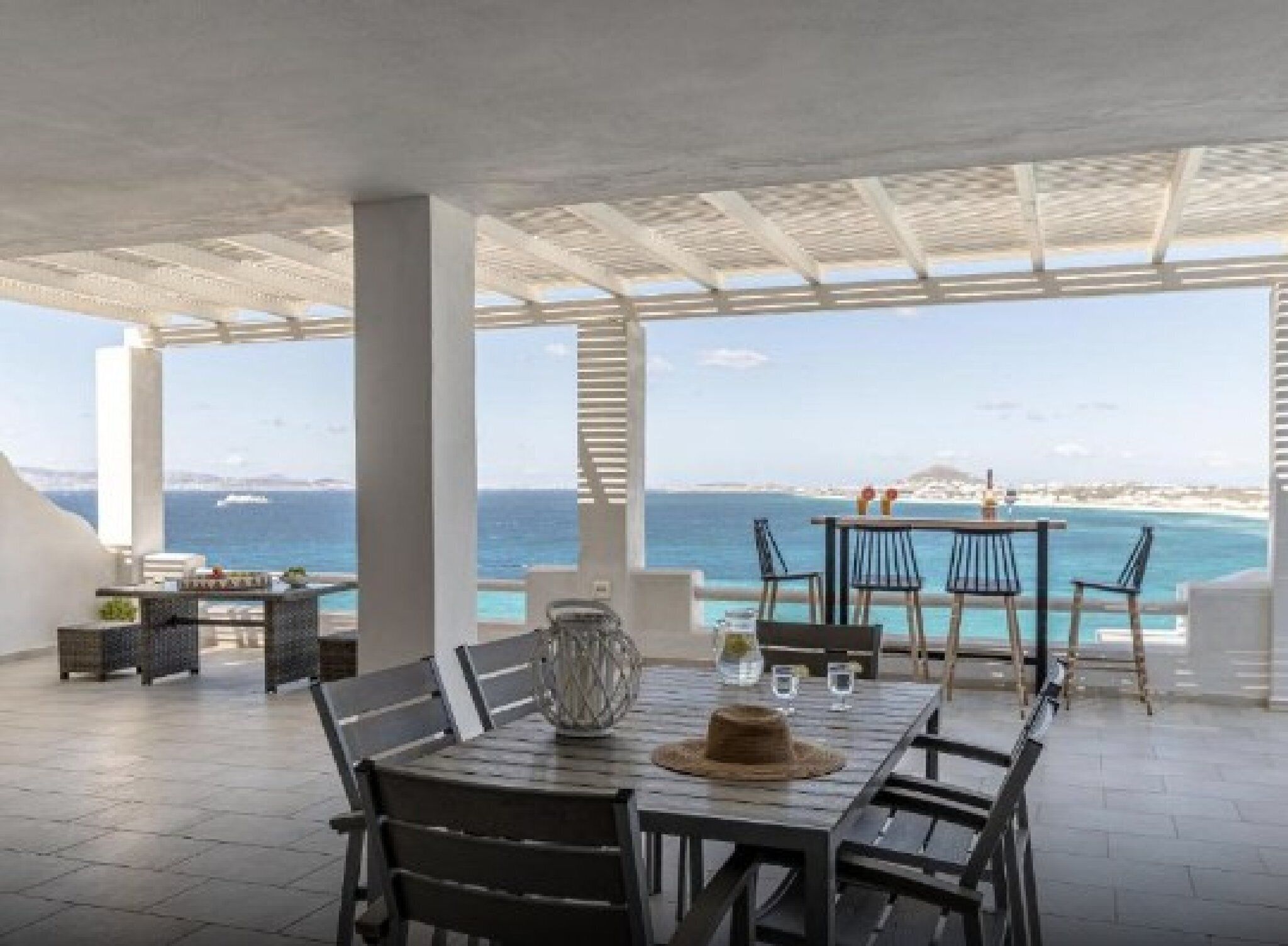Un espace extérieur aménagé pour les repas, offrant une vue sur la mer, avec une table, des chaises et un vase décoratif.