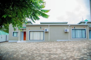 A building with a tiled patio, two air conditioning units, and a door with a curtain.