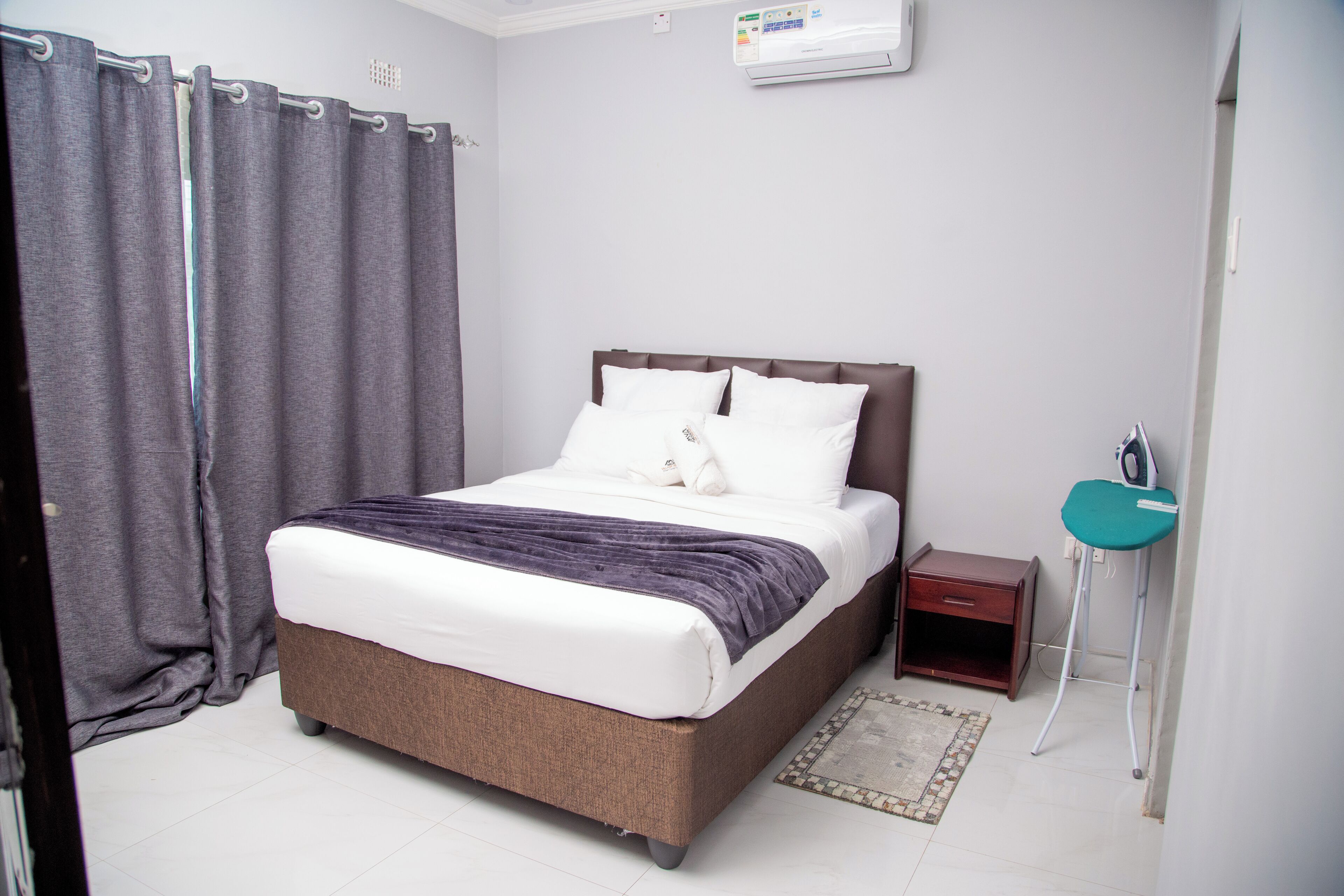 Une chambre d’hôtel comprenant un lit, une table de chevet, une petite armoire, un miroir dans la salle de bain et un rideau de douche.