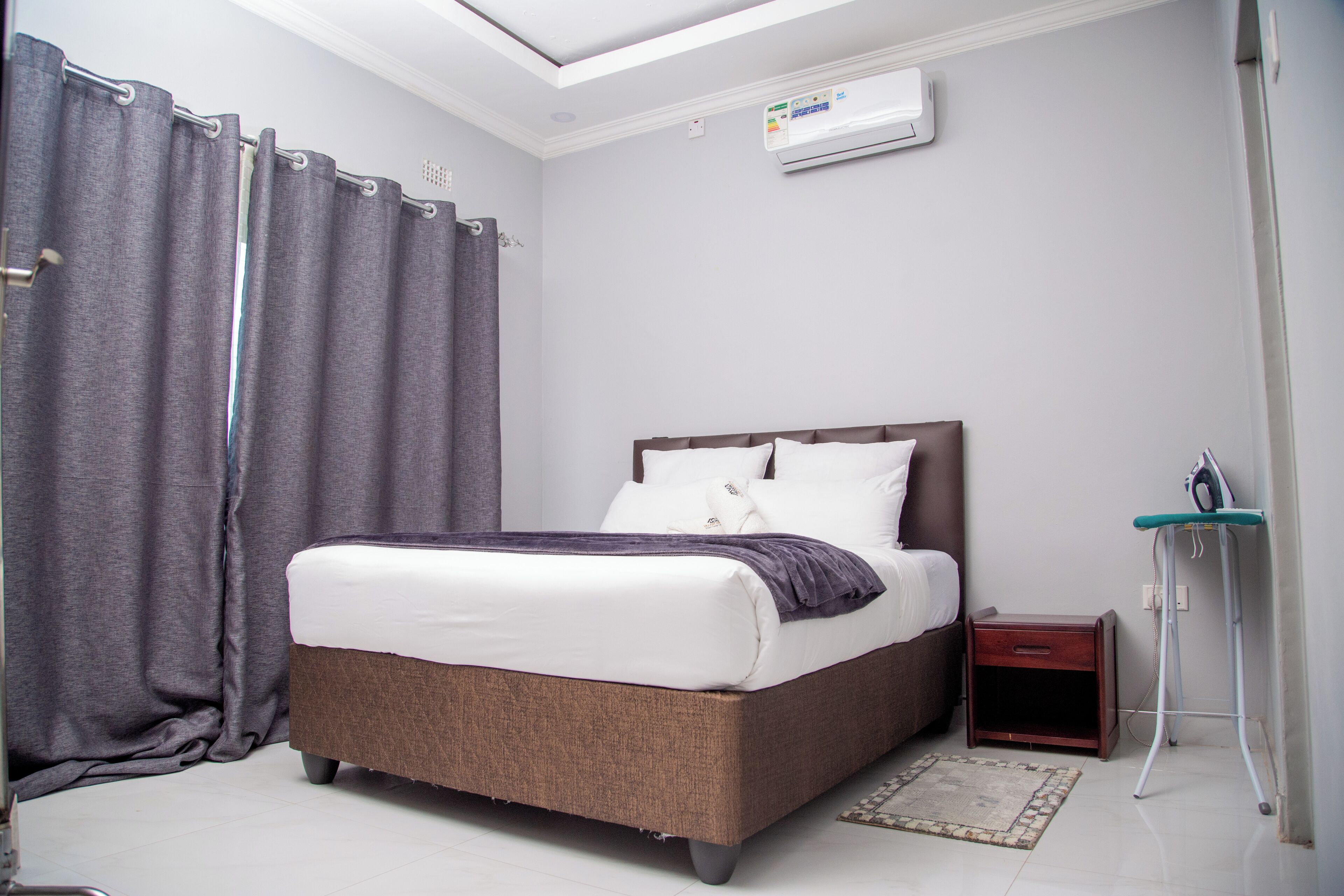 A bedroom with a bed, a bedside table, a nightstand, an iron, and a ceiling fan.