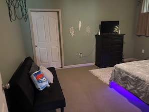 A bedroom with a bed, a dresser, a television, and a wall with decorative leaves.