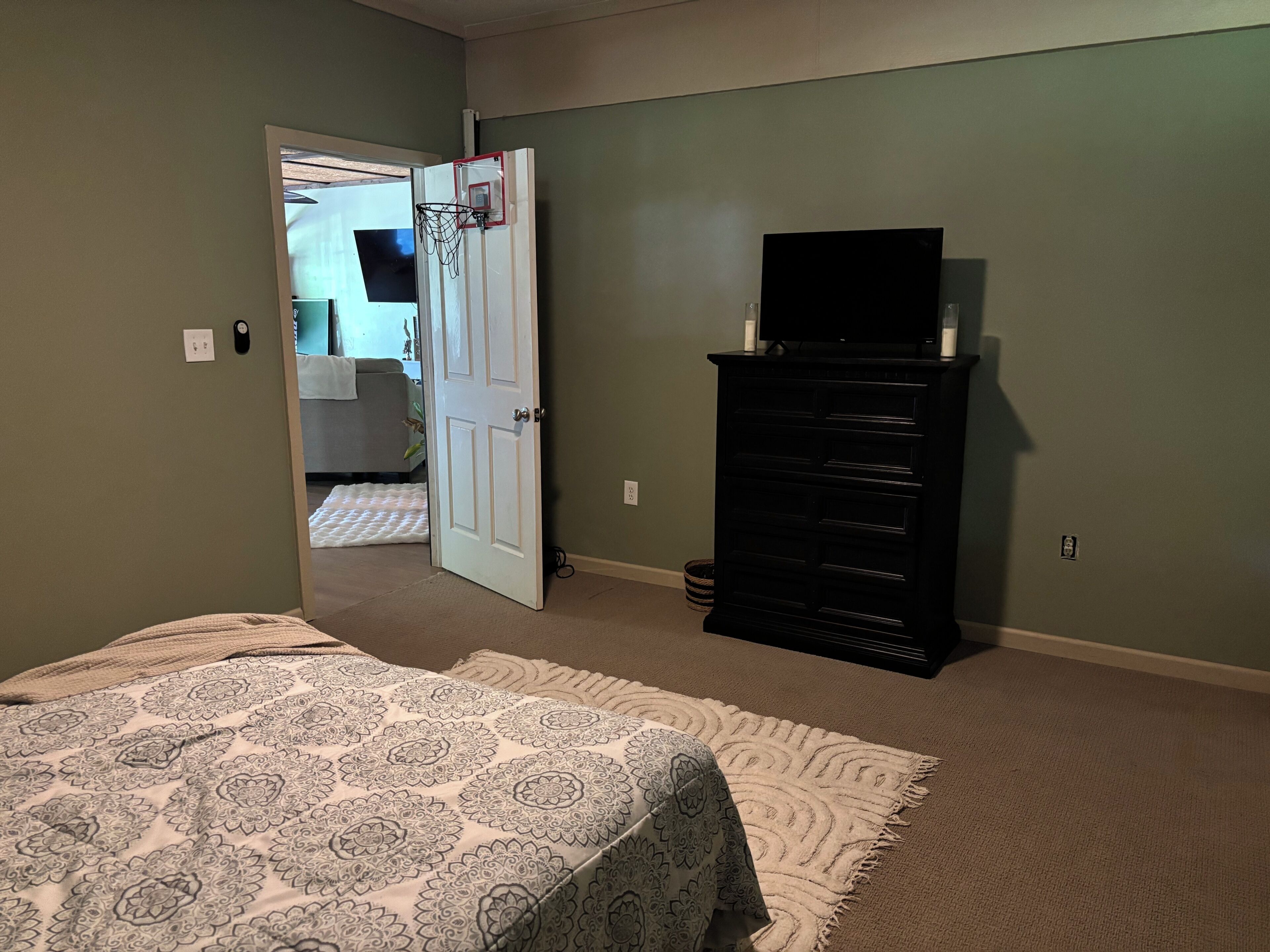 Un dormitorio con cama, cómoda, televisor y puerta que da a otra habitación.