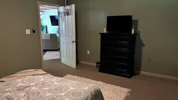 Un dormitorio con cama, cómoda, televisor y puerta que da a otra habitación.