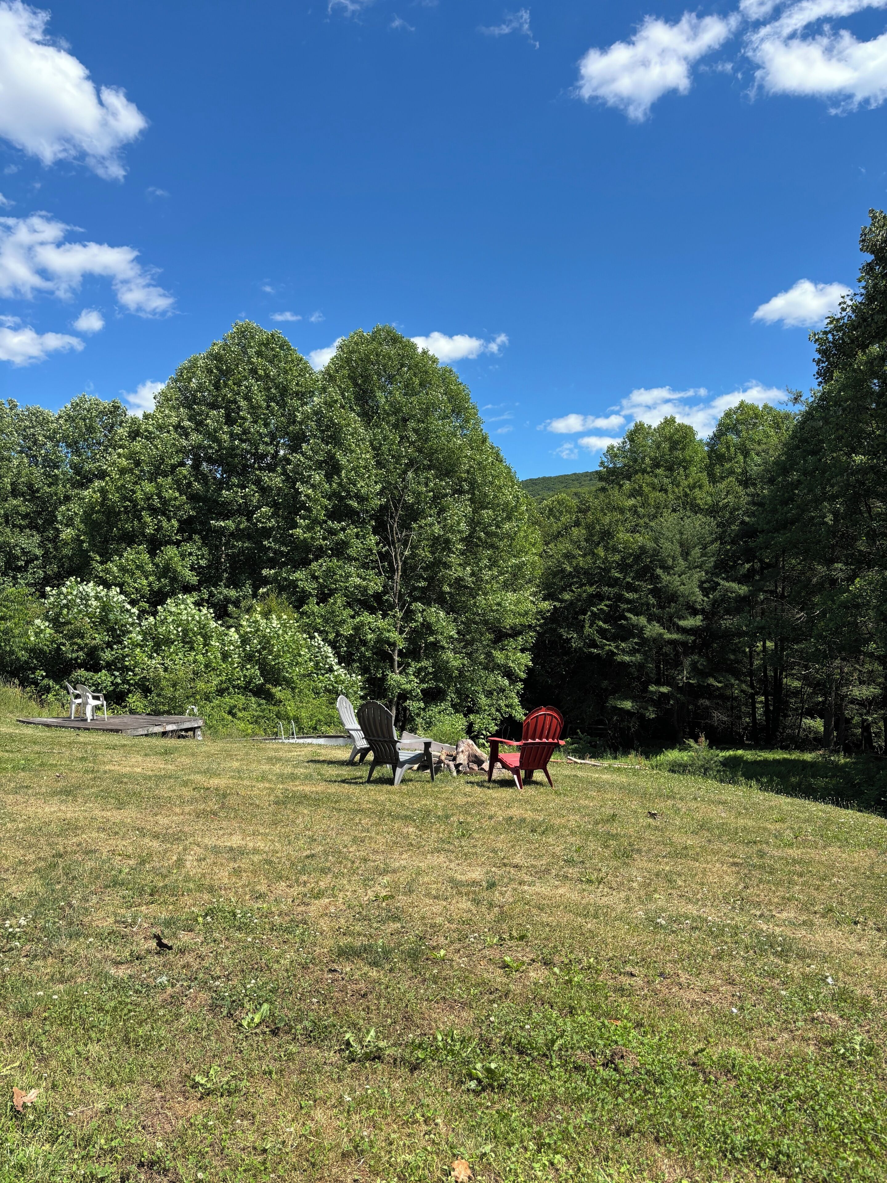 Un espacio al aire libre con césped, sillas Adirondack y una terraza de madera.