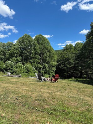 A grassy outdoor area with Adirondack chairs and a wooden deck.