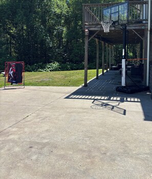 A basketball court with a hoop, a covered seating area, and a sign with a baseball player.