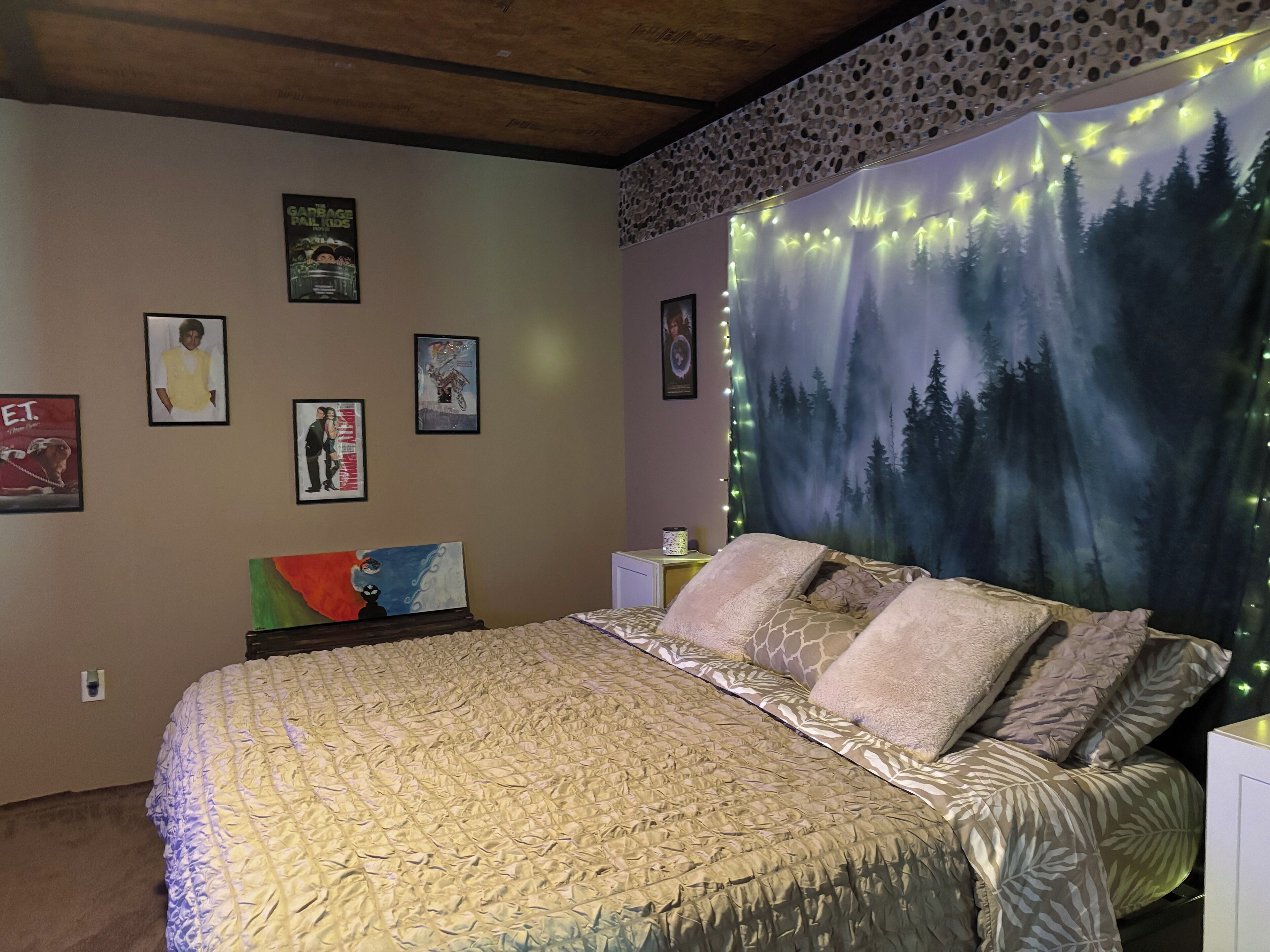 Une chambre avec un grand lit, une tapisserie sur le thème de la forêt et divers affiches accrochées au mur.