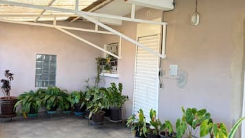 A covered patio area with potted plants, a ceiling fan, and a white door.