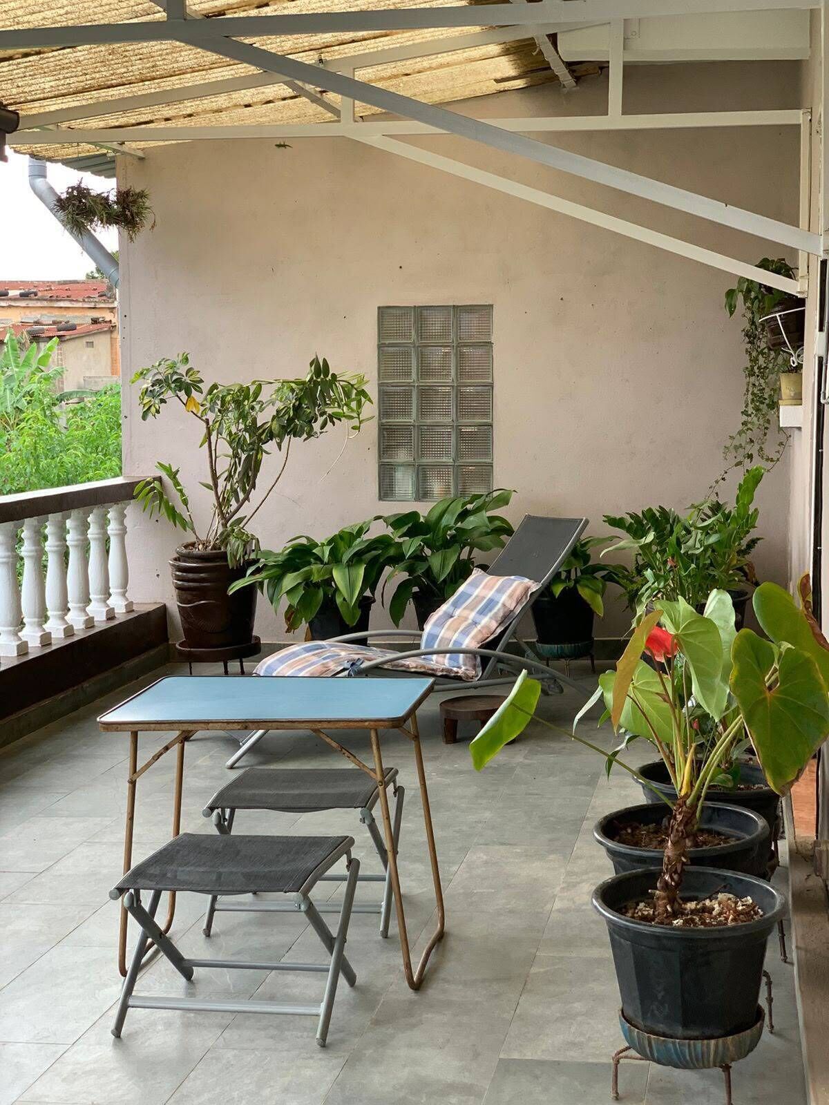 Un espace extérieur aménagé, abrité et doté de fauteuils et d’une table, le tout entouré de plantes en pot.
