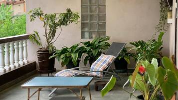 Un espace extérieur aménagé, abrité et doté de fauteuils et d’une table, le tout entouré de plantes en pot.