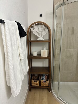 Un baño con toallero blanco, repisa de madera con artículos de aseo y cabina de ducha de cristal.
