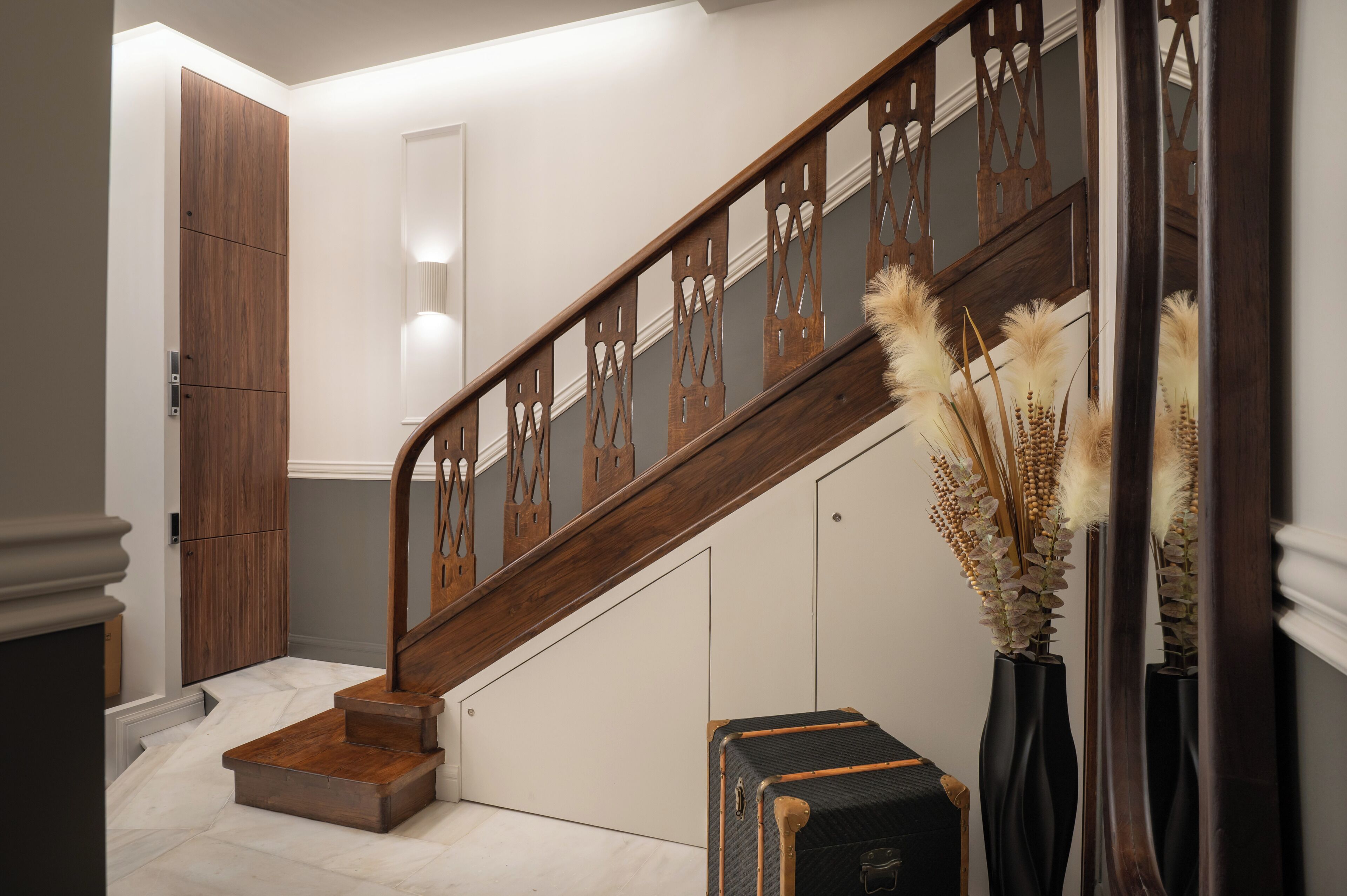 Un escalier en bois avec une rampe, un luminaire fixé au mur et un vase contenant des plantes séchées.