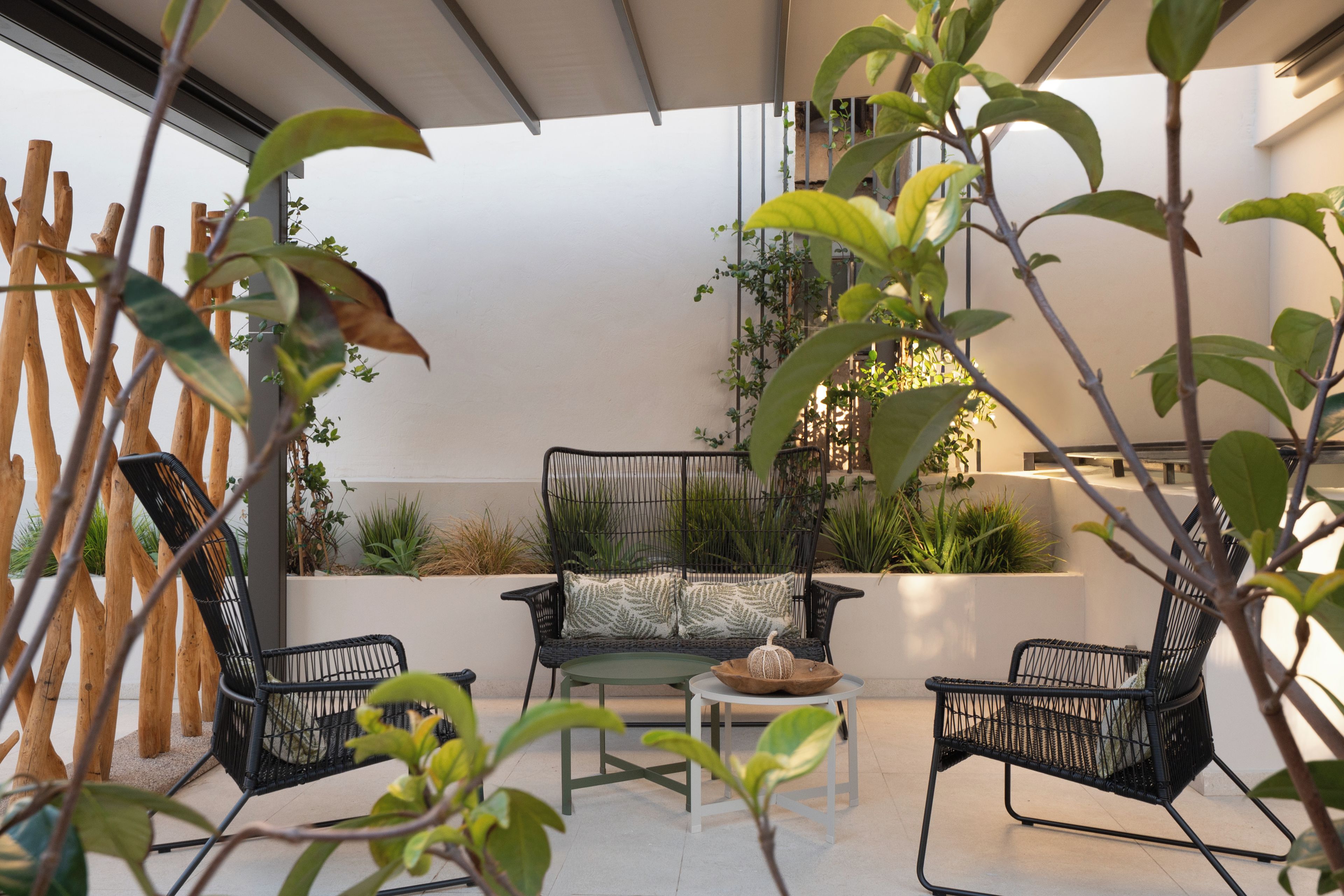 A modern outdoor seating area with two black wicker chairs, a small round table, and a white planter with a decorative object.
