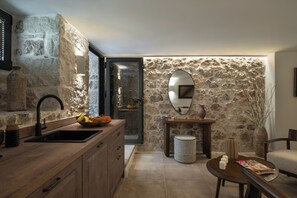 Uma cozinha com parede de pedra, bancada de madeira, pia e espelho.