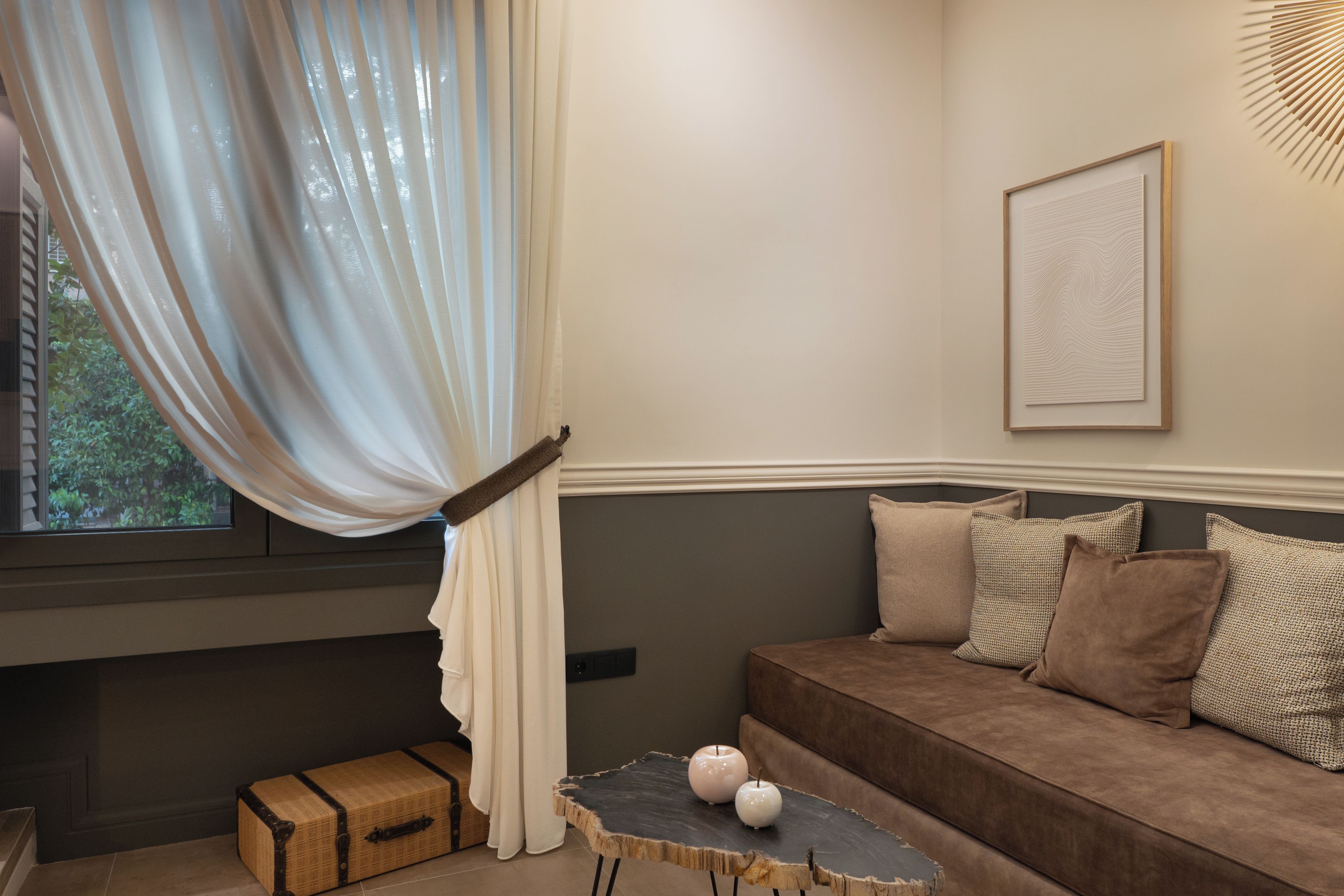A cozy room with a brown sofa, a small table with candles, and a window with sheer curtains.