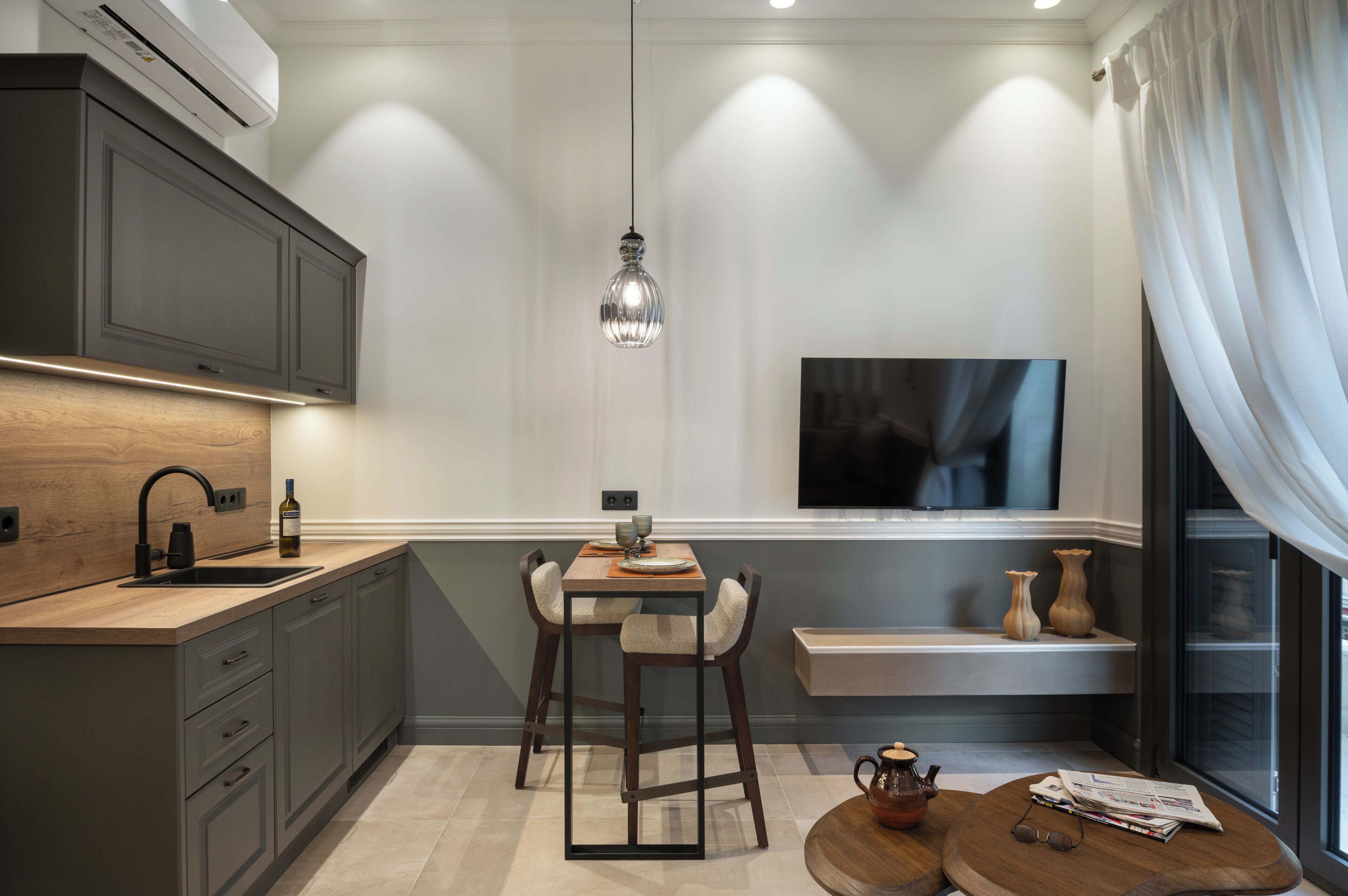 Une cuisine moderne avec un coin repas, un téléviseur fixé au mur et une fenêtre avec des rideaux.