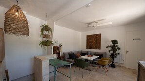 Een moderne woonkamer met een bank, een eettafel en stoelen. Er is een plafondventilator, een hanglamp en een potplant.