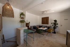 Ein modernes Wohnzimmer mit einer Couch, einem Esstisch und Stühlen. Es gibt einen Deckenventilator, eine Hängelampe und einen Topfpflanzen.