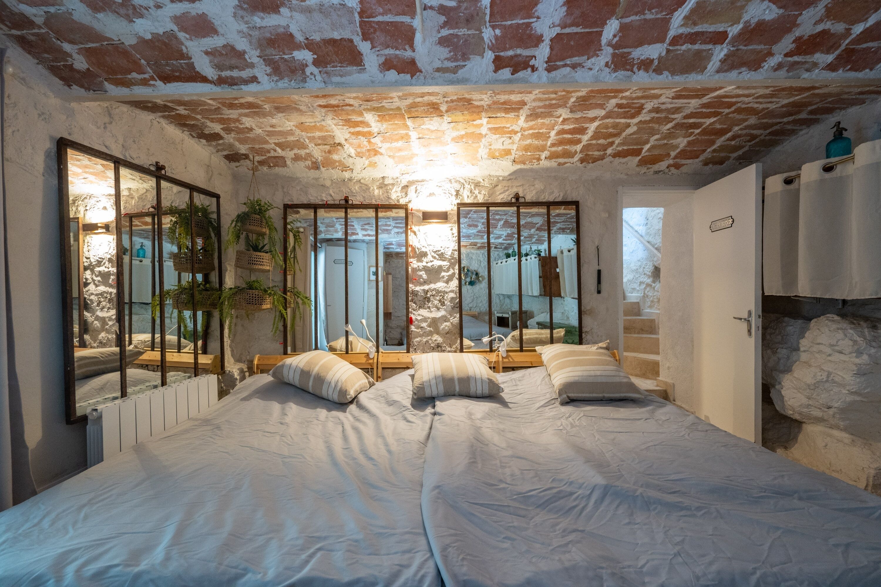 A bedroom with a brick ceiling, two beds, a mirror, and a view of a stone wall.