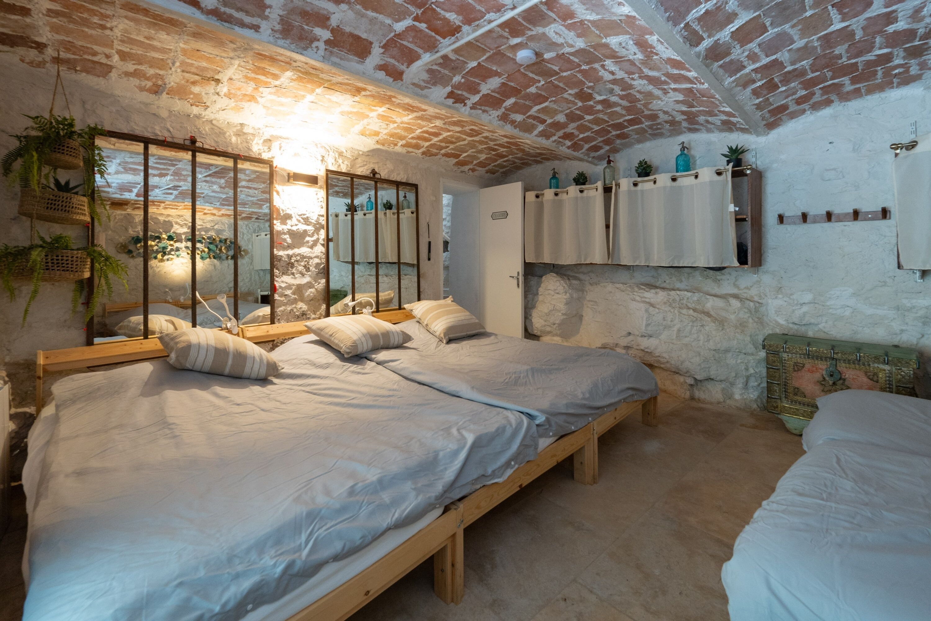 A bedroom with two beds, a brick ceiling, and a stone wall.