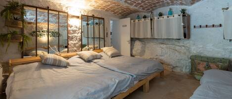 A bedroom with two beds, a brick ceiling, and a stone wall.