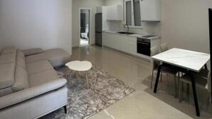 Uma sala de estar moderna com um sofá, uma mesa redonda pequena e um espaço de jantar com mesa e cadeiras.