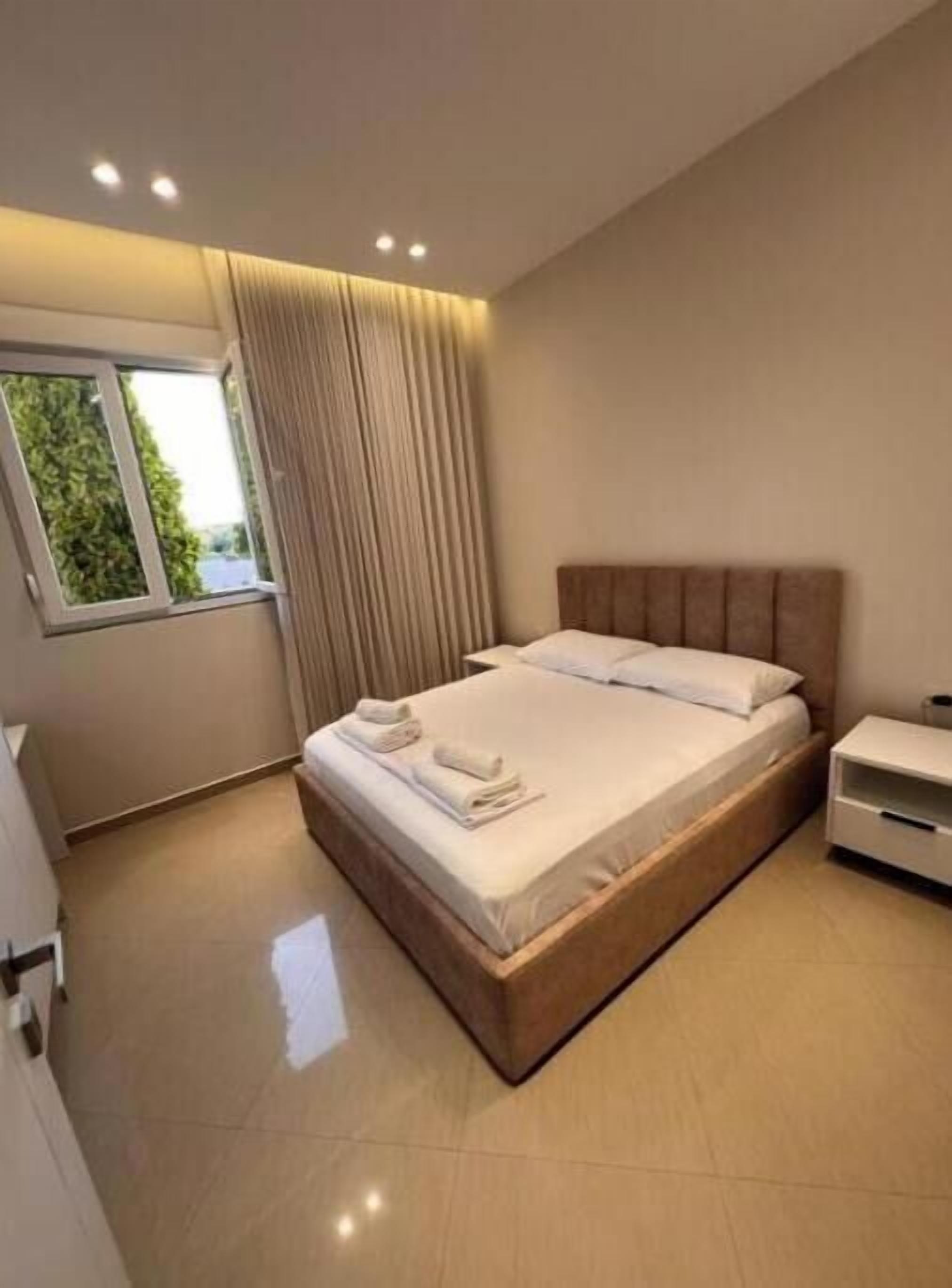 A modern bedroom with a large bed, a nightstand, and a window with curtains.