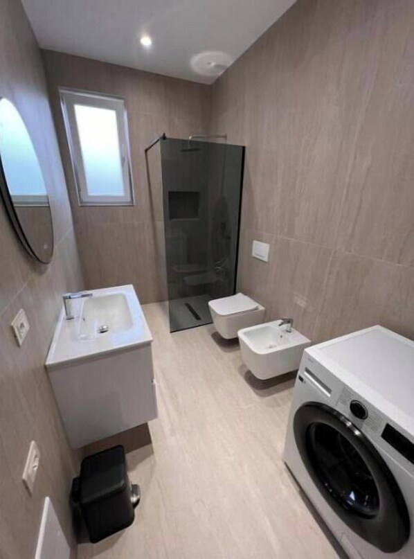 A modern bathroom with a glass shower enclosure, a washing machine, and a sink.