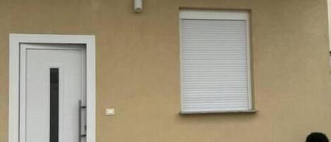 Fachada de edificio con una puerta cerrada, una ventana con persiana y una planta en maceta.