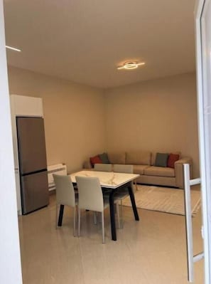 A compact living space with a kitchenette, a dining table with chairs, and a sofa with cushions.