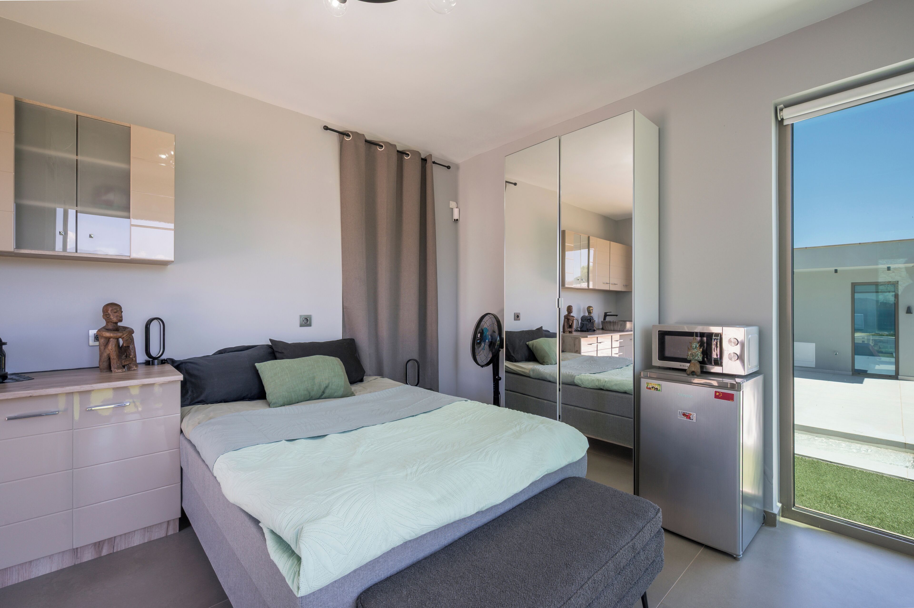 Et moderne soveværelse med seng, natbord, kommode, spejl og udsigt til en balkon.