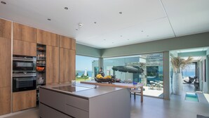 Una cocina moderna con una isla central, horno integrado y vistas al océano a través de amplios ventanales.