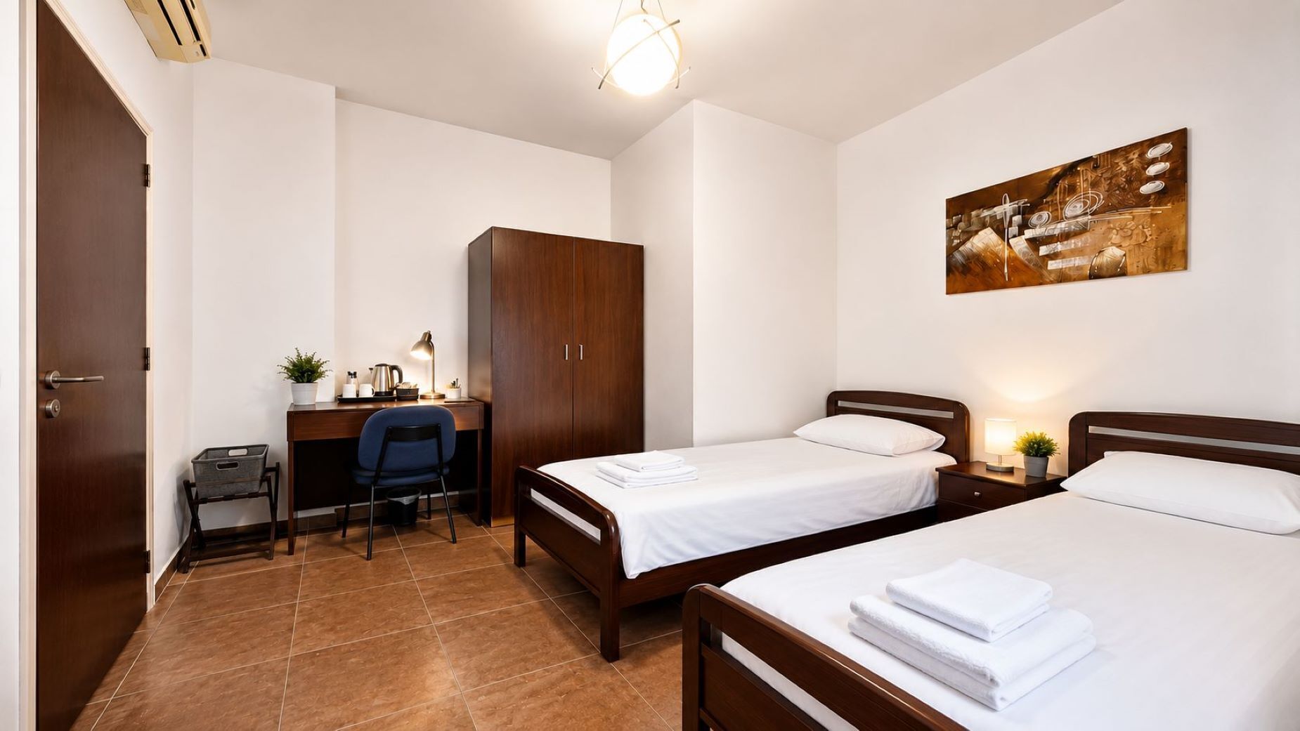 Une chambre d’hôtel avec deux lits, un bureau avec une chaise, une armoire et un tableau au mur.