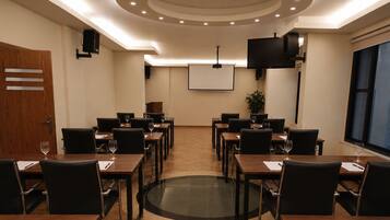 Una sala de conferencias con una pantalla grande, varias mesas con sillas y una puerta de madera.