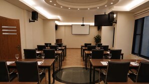 Une salle de conférence dotée d’un grand écran, de plusieurs tables avec des chaises et d’une porte en bois.