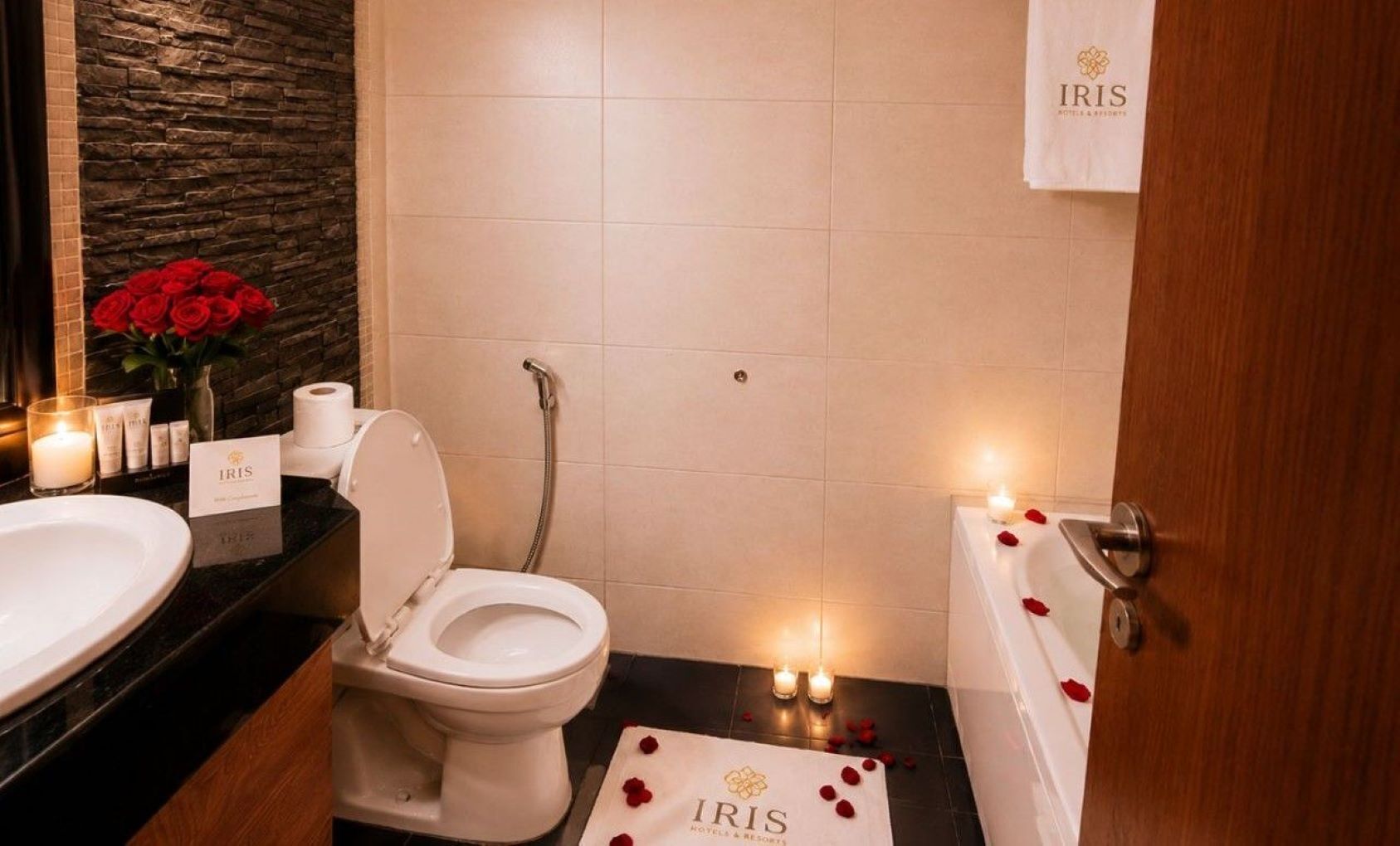 A bathroom with a toilet, a sink, a bathtub, and a shower. There are candles and rose petals on the floor.