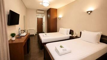 A hotel room with two beds, a desk with a flat-screen TV, a small plant, and a wall-mounted light fixture.
