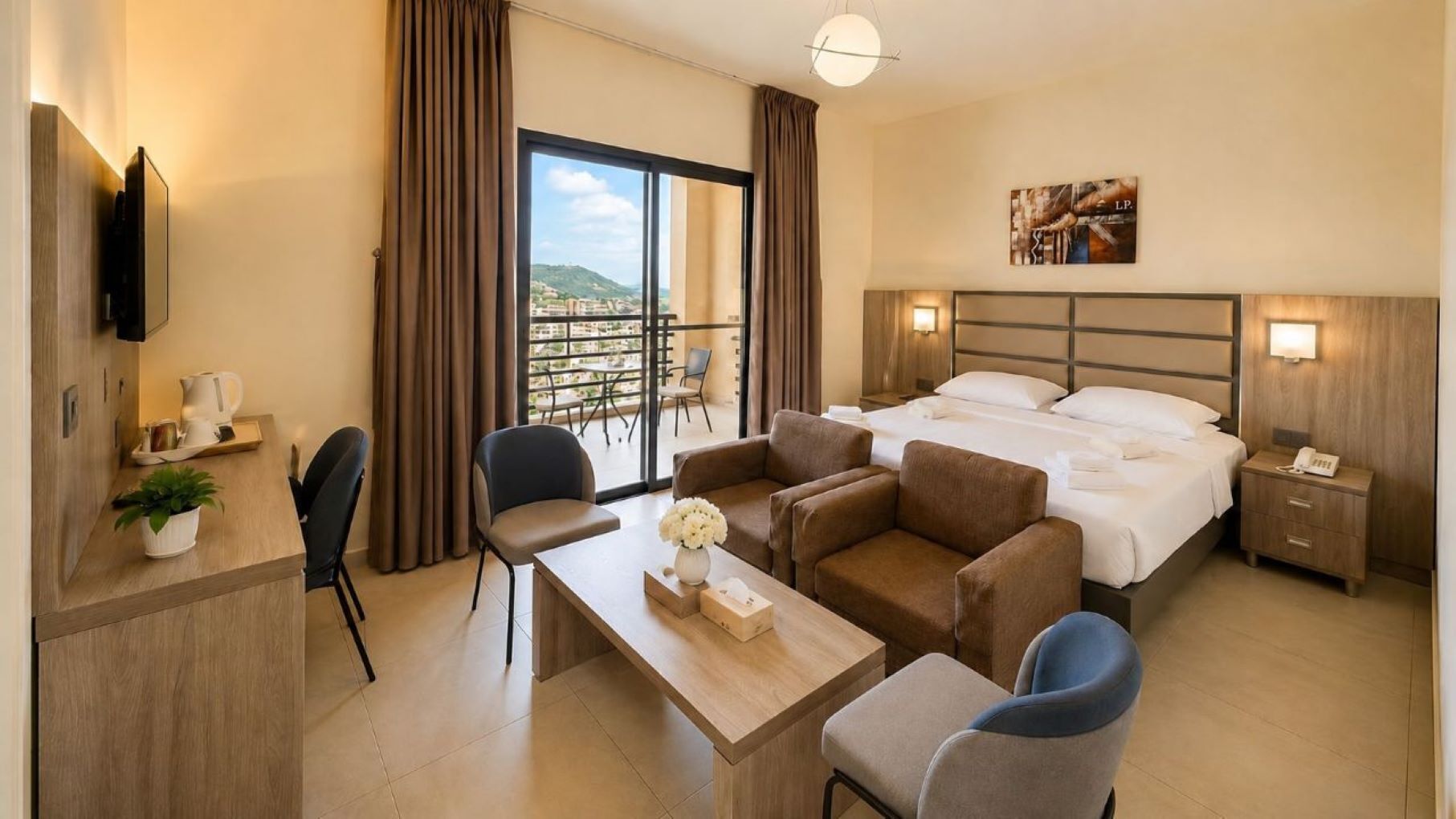 Habitación de hotel con cama, sofá, escritorio, silla, televisión, balcón con vistas y un cuadro en la pared.