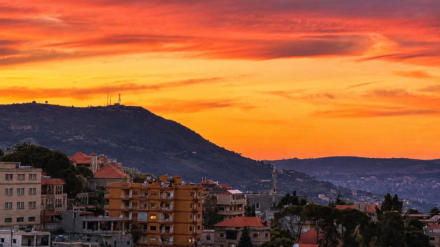 A cityscape with buildings and a hill in the background during sunset.