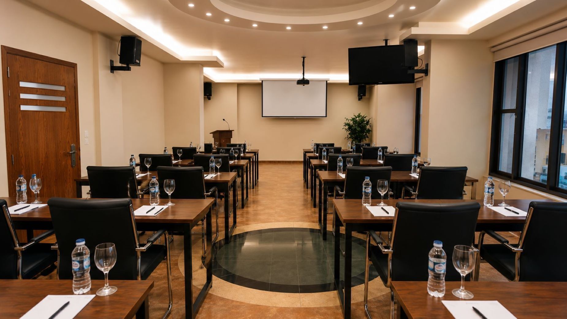 A conference room with multiple tables, chairs, a projector screen, and a large window.