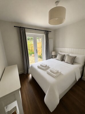 Ein Schlafzimmer mit einem Bett, Nachttischen, einer Lampe und Blick ins Freie.