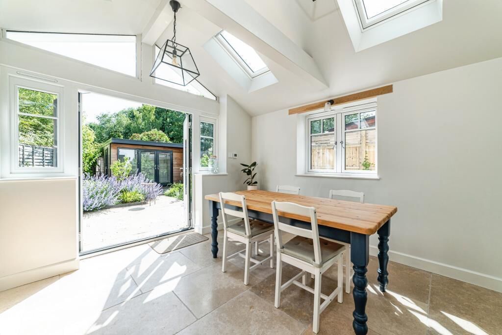 A dining area with a wooden table and chairs, large windows, and a view of the garden.