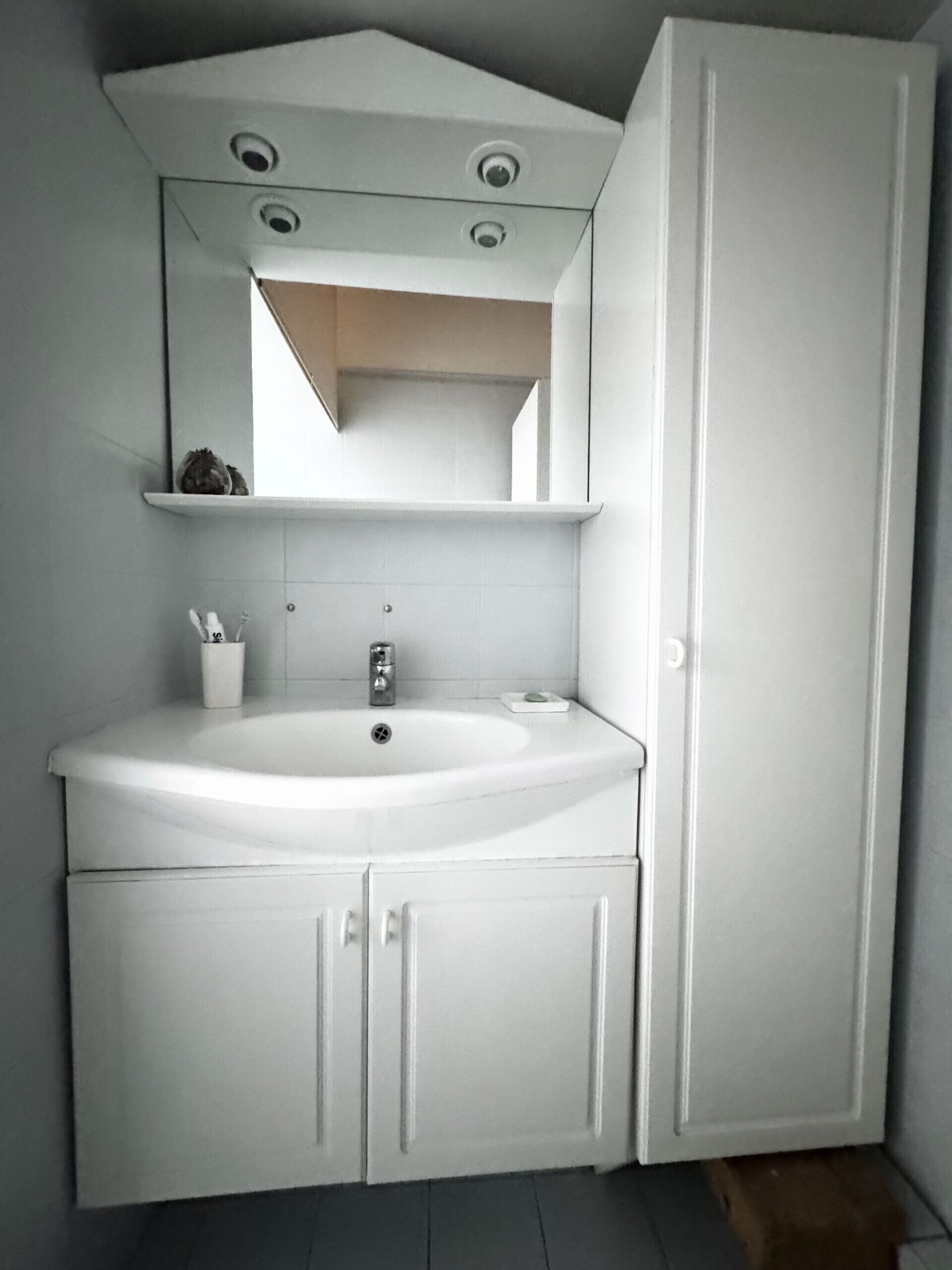 A bathroom with a white sink, mirror, and cabinets.