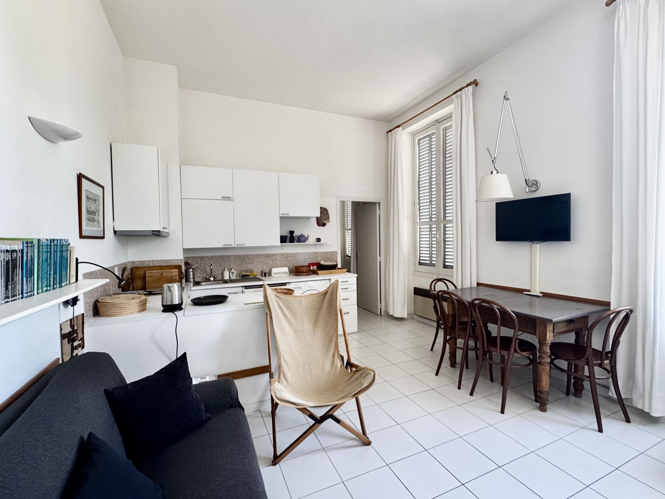 A modern kitchen with white cabinets, a dining table with chairs, a sofa, and a TV.