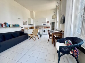 Ein modernes Wohnzimmer mit einer Couch, einem Esstisch mit Stühlen, einer Küchenzeile und einem großen Fenster.