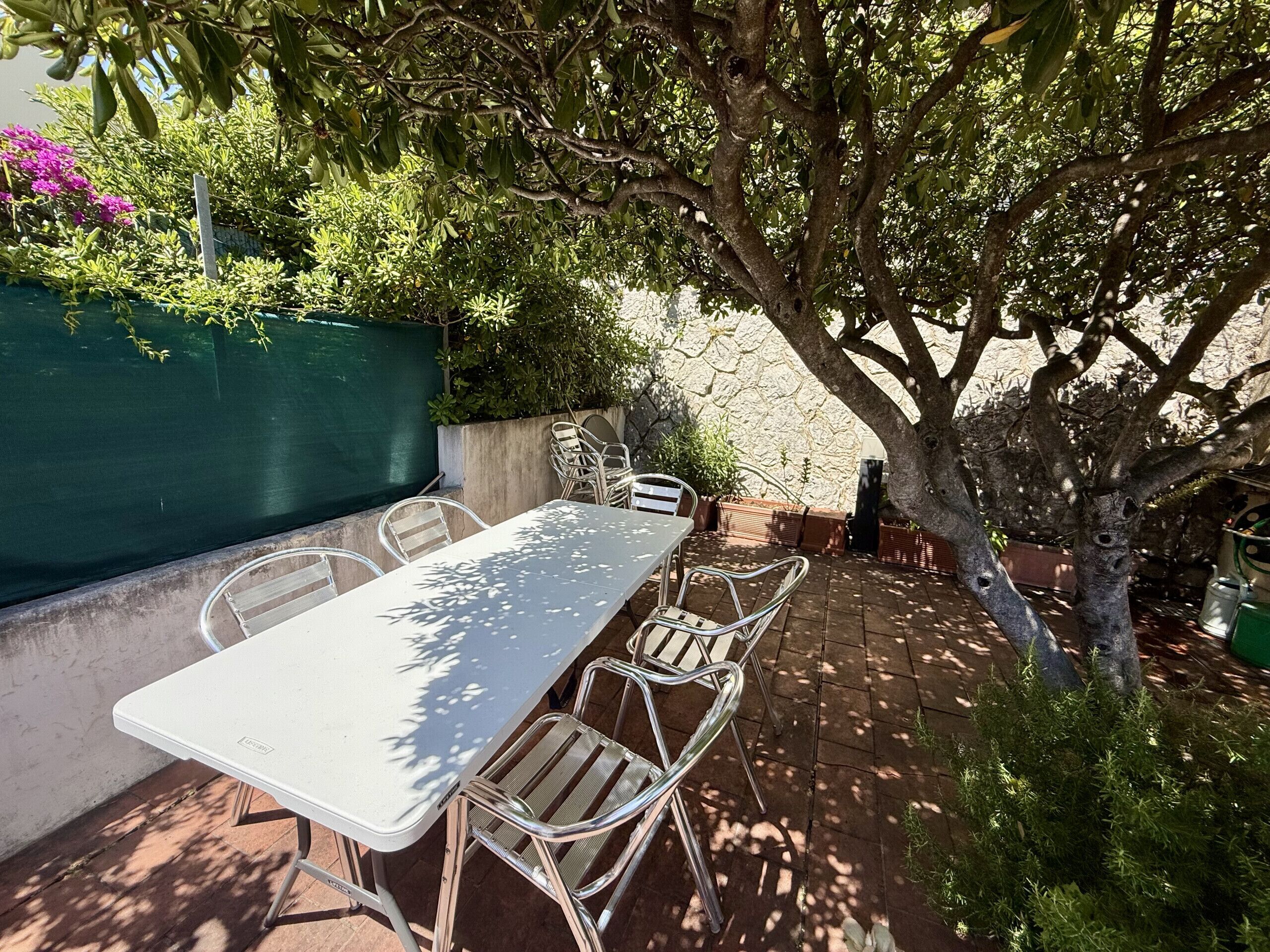 Patio esterno con tavolo e sedie, immerso nel verde e alberato.