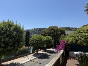 Eine Straße mit Leitplanke, Bäumen und einer Hügellandschaft im Hintergrund.