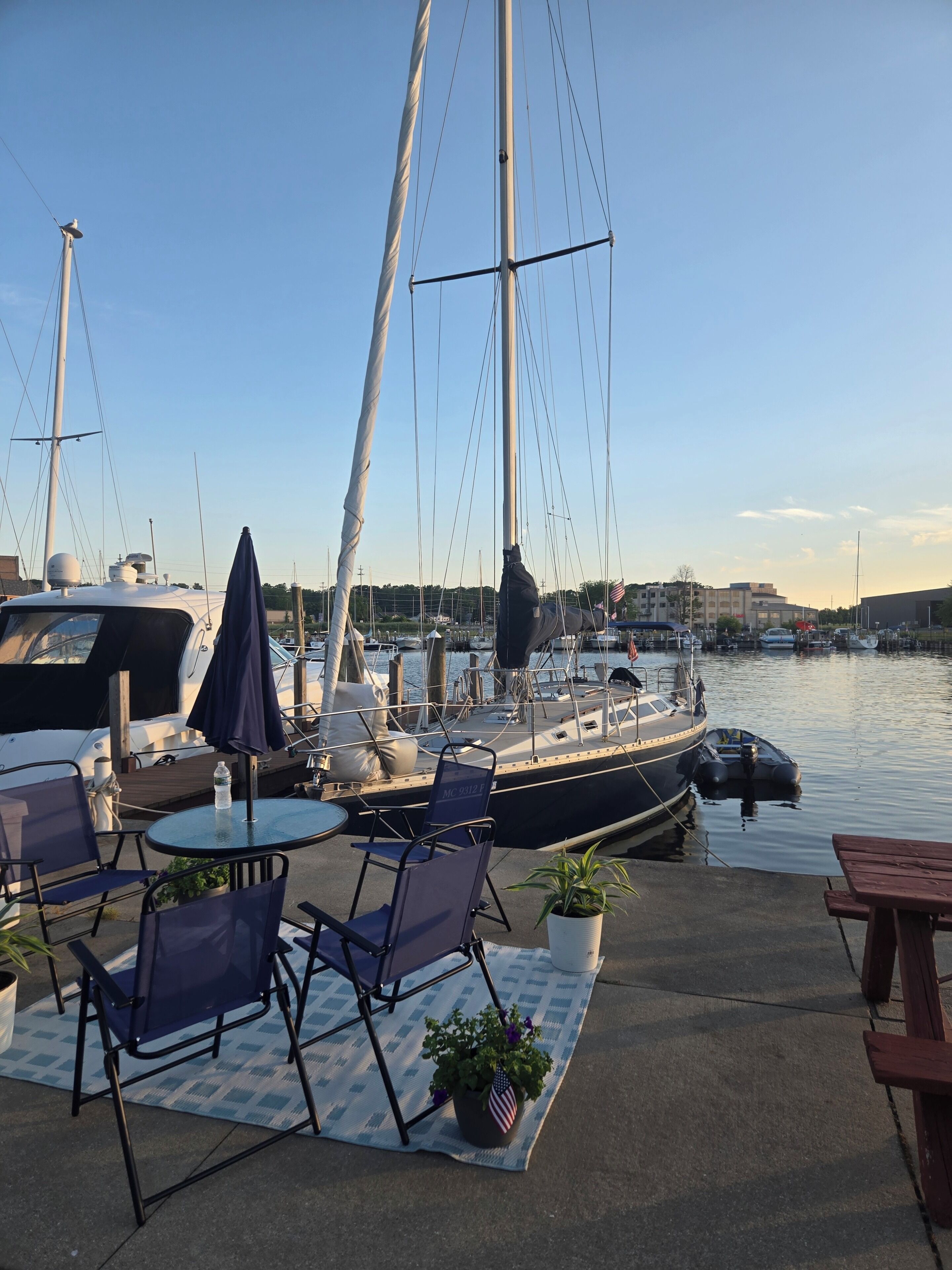 A marina with boats docked, outdoor seating with umbrellas, and a clear sky.